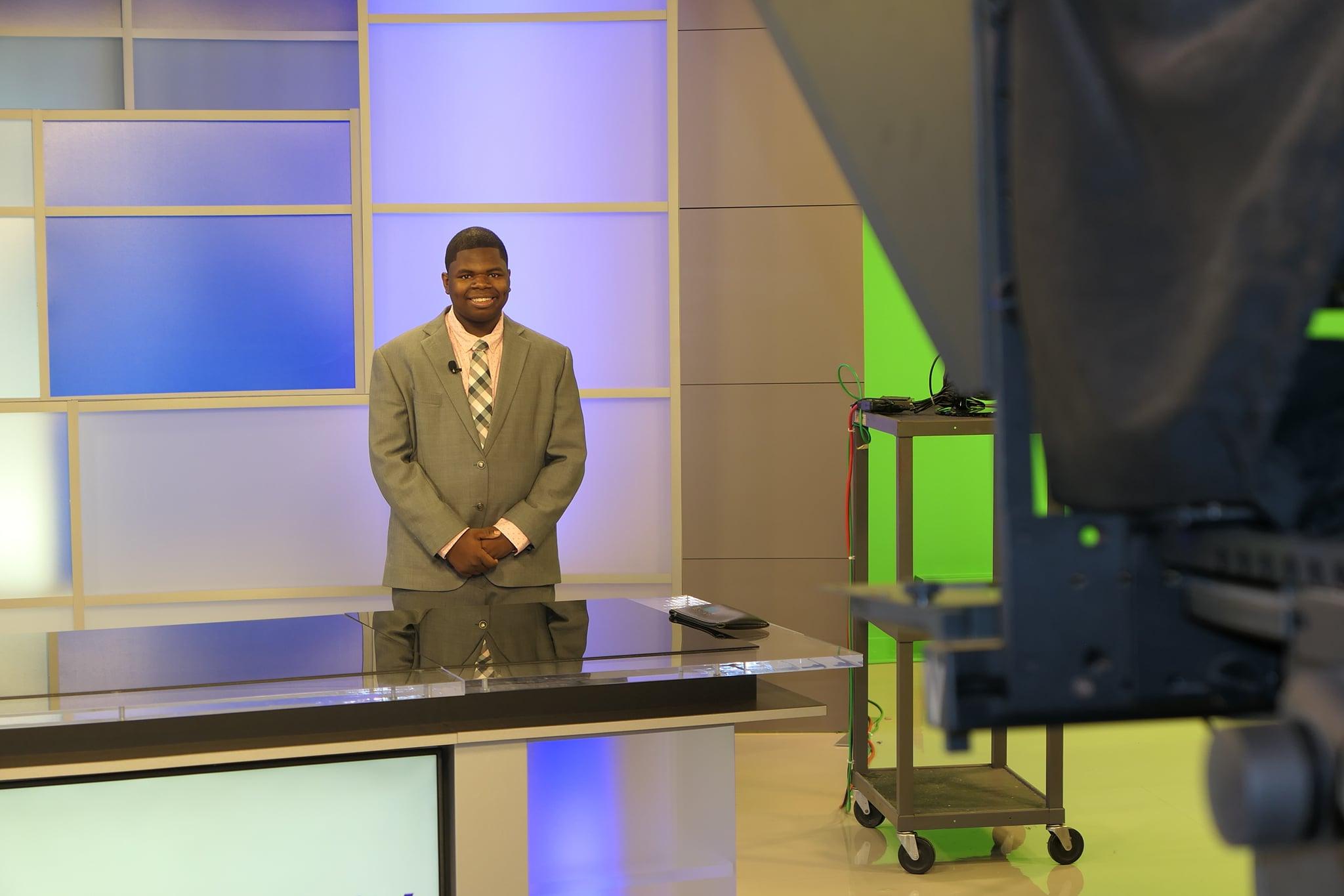 Broadcasting student in front of the camera reporting the news in a suit and tie